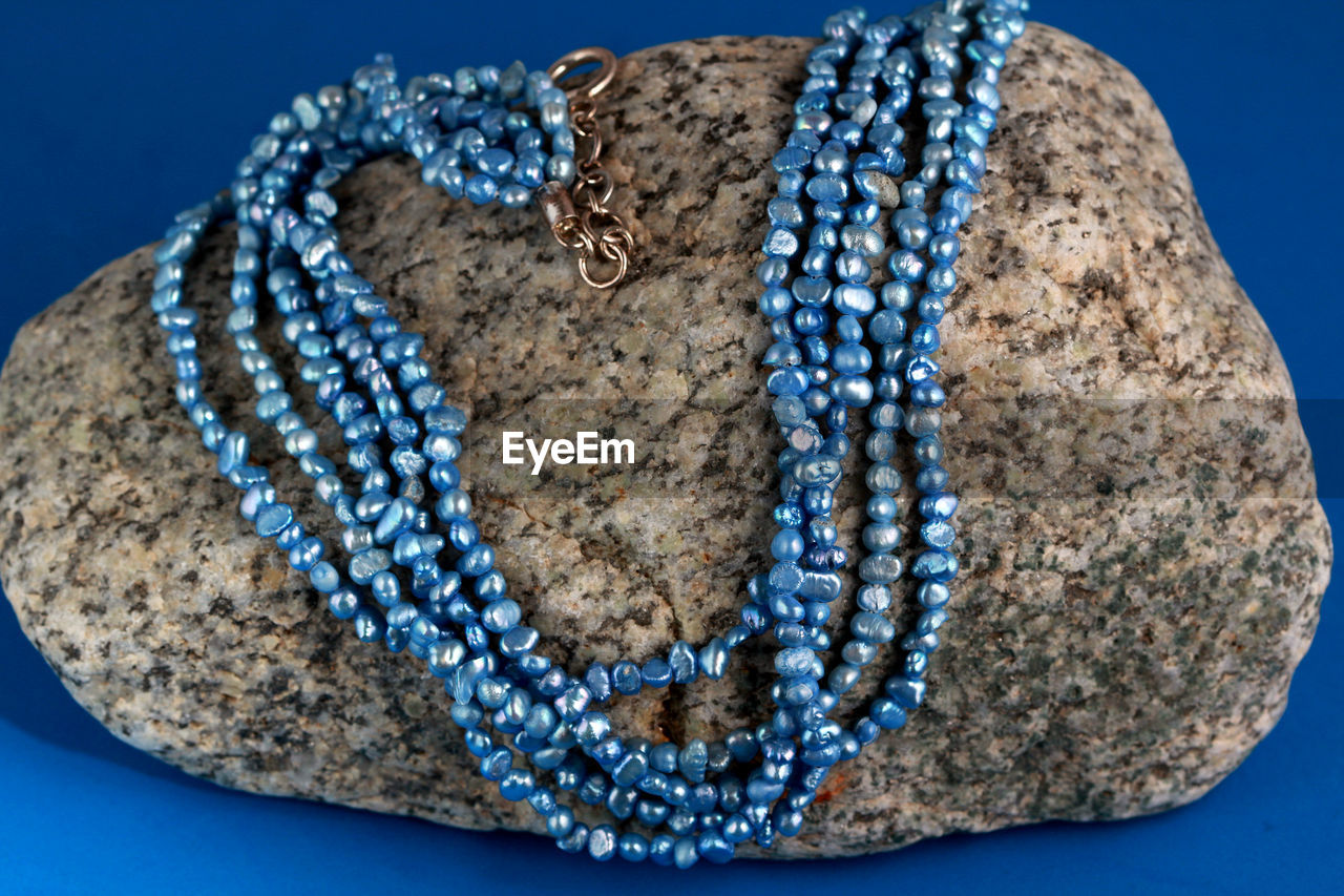 Strings of blue freshwater pearls displayed on a granite rock against a blue background