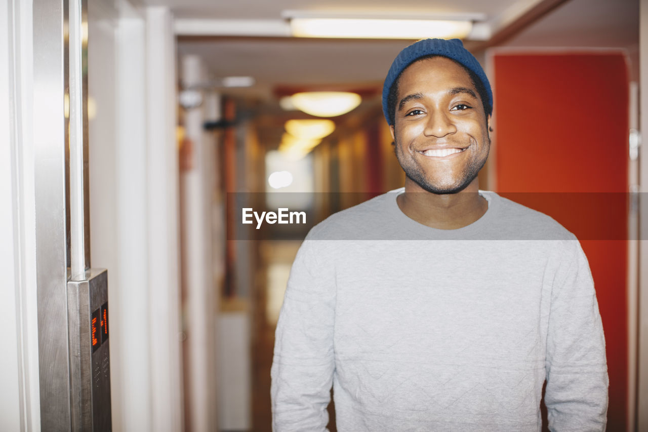 Portrait of happy man standing in college dorm corridor