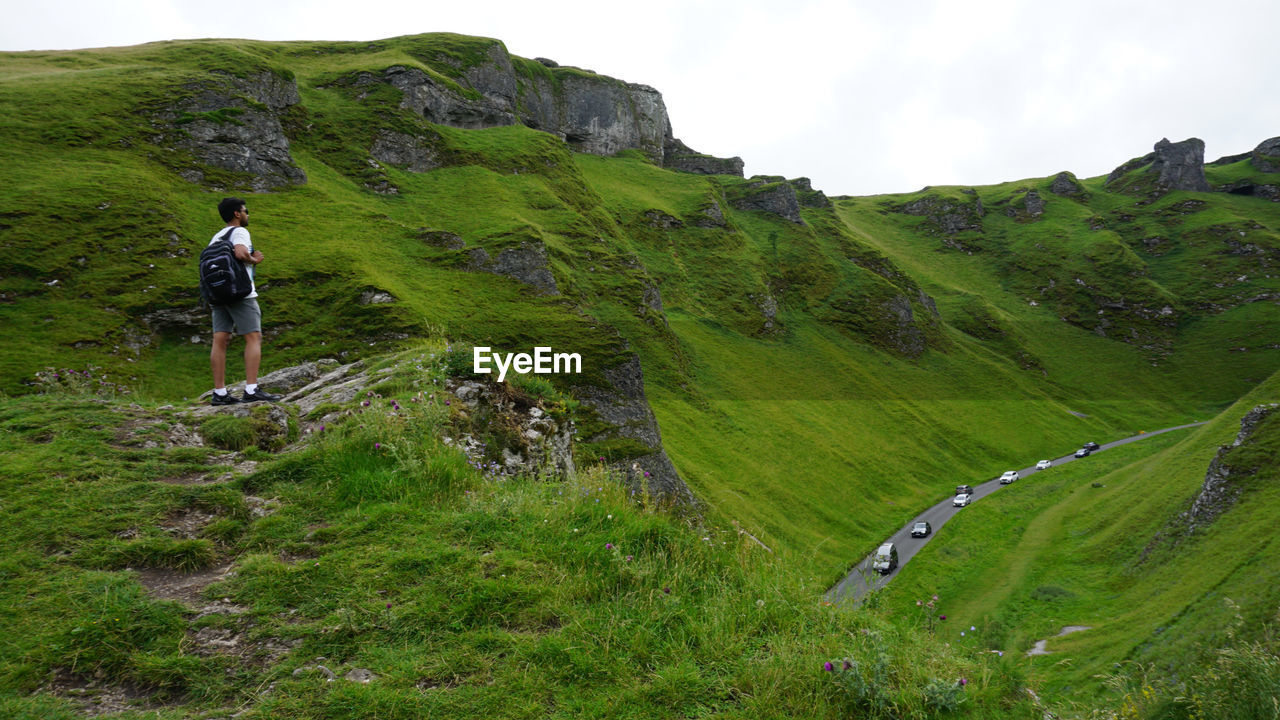 Rear view of man standing on high mountain against sky with road below