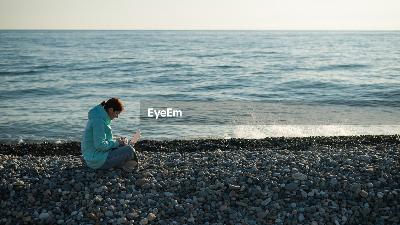 Side view of woman using laptop at beach