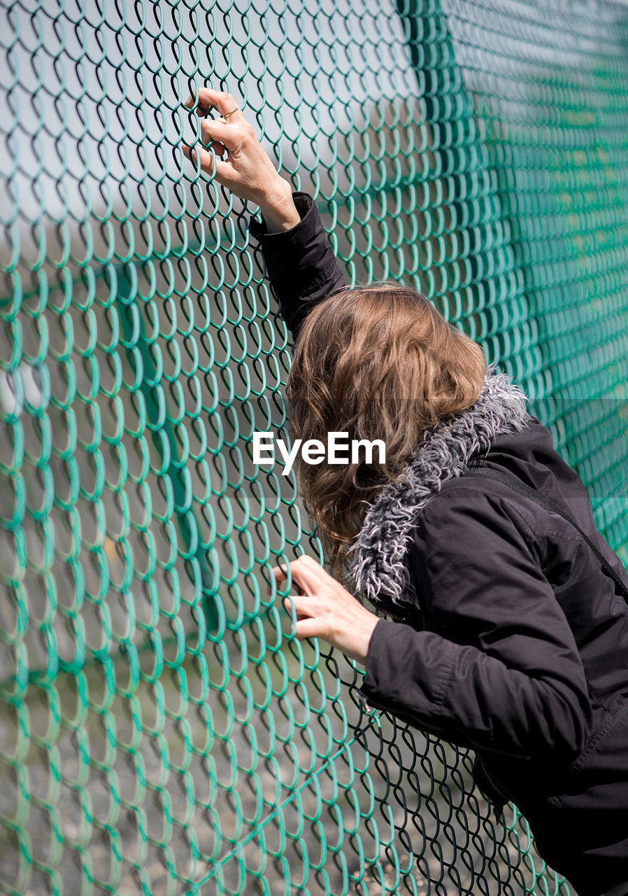 Woman looking through green chainlink fence