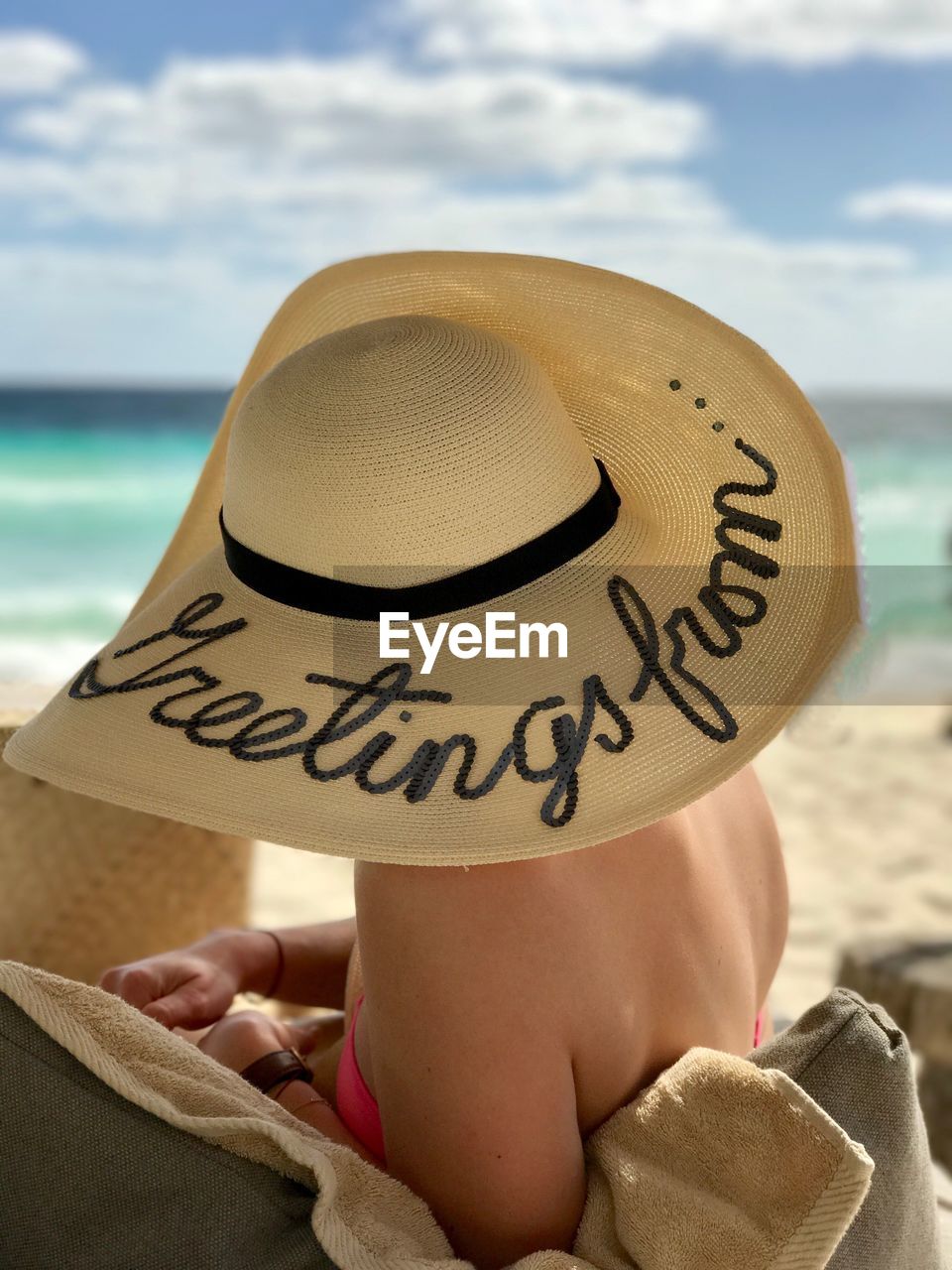 Close-up of woman with text on hat relaxing at beach against sky