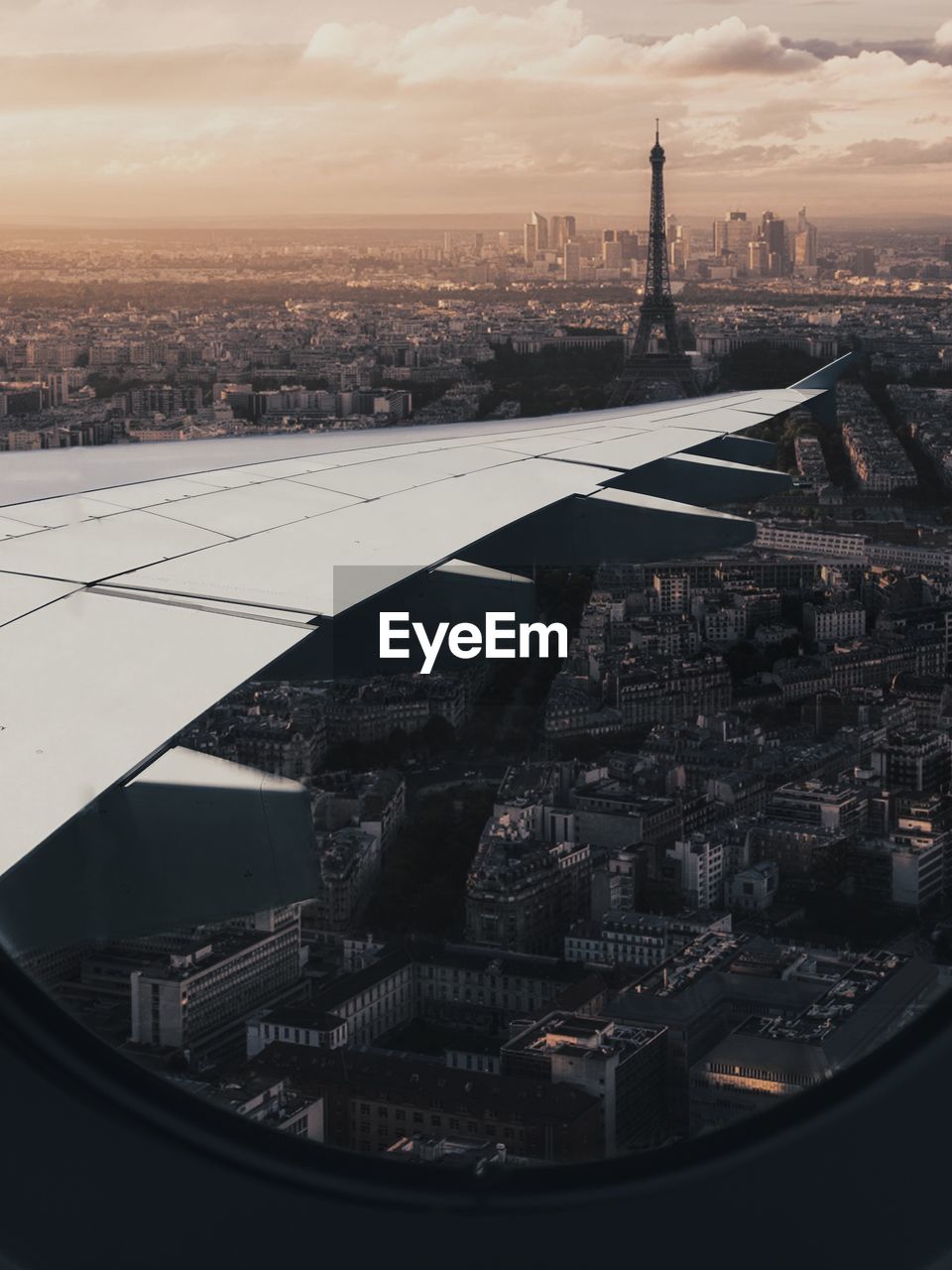 Cropped image of airplane wing over cityscape seen through window during sunset