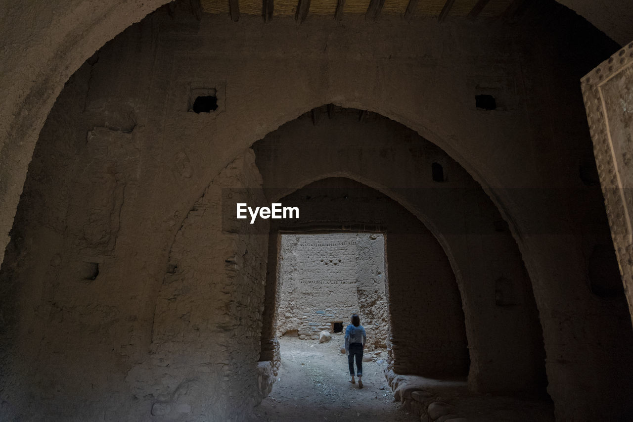 Rear view of woman walking below arch at old ruin