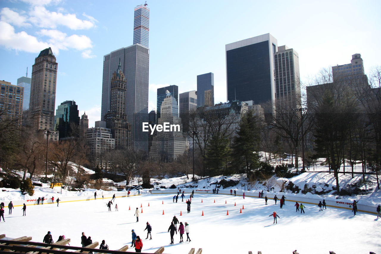 People ice-skating on snow field against buildings