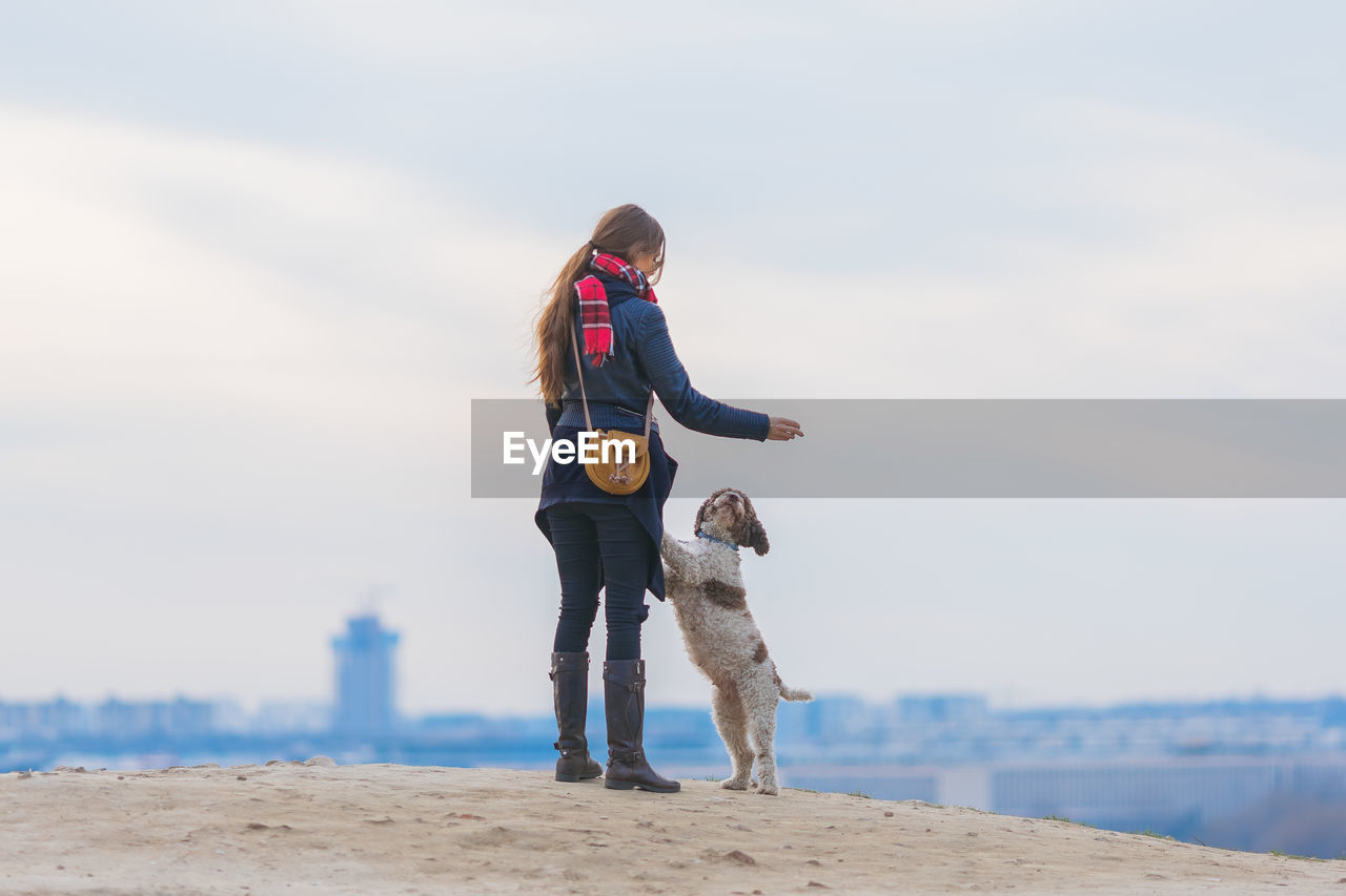 Woman standing with dog on hill against sky