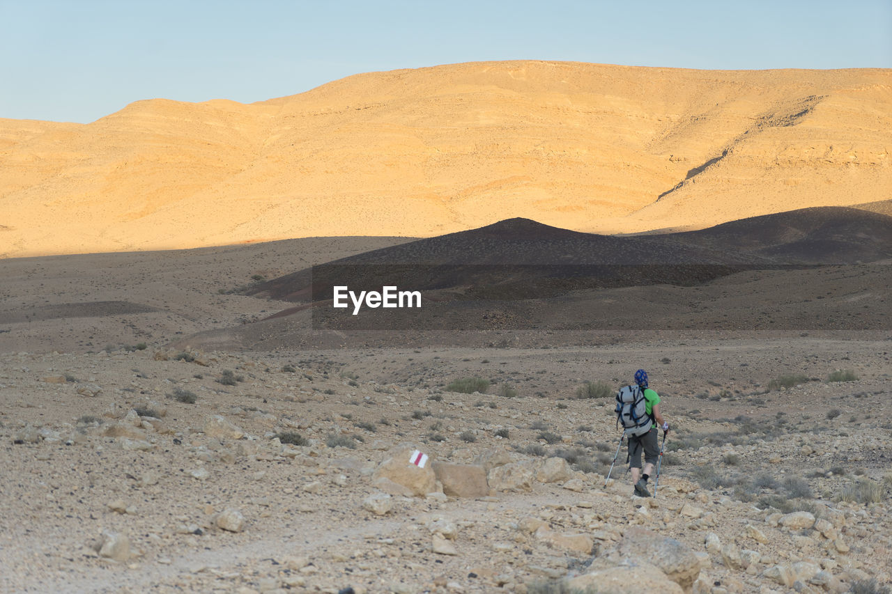 MAN WALKING ON DESERT AGAINST MOUNTAIN