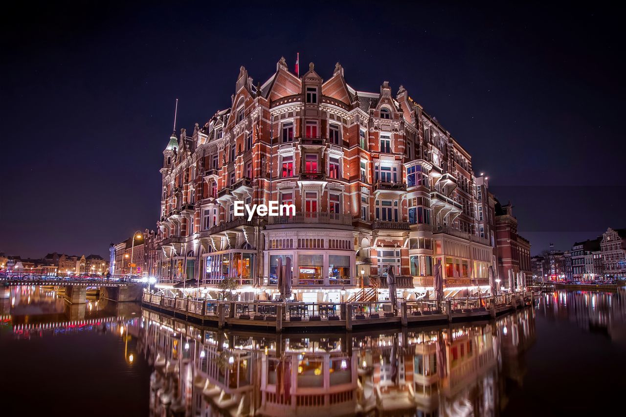 Illuminated building reflecting on lake at dusk