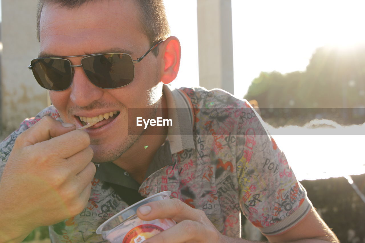 PORTRAIT OF YOUNG MAN WEARING SUNGLASSES HOLDING CAMERA