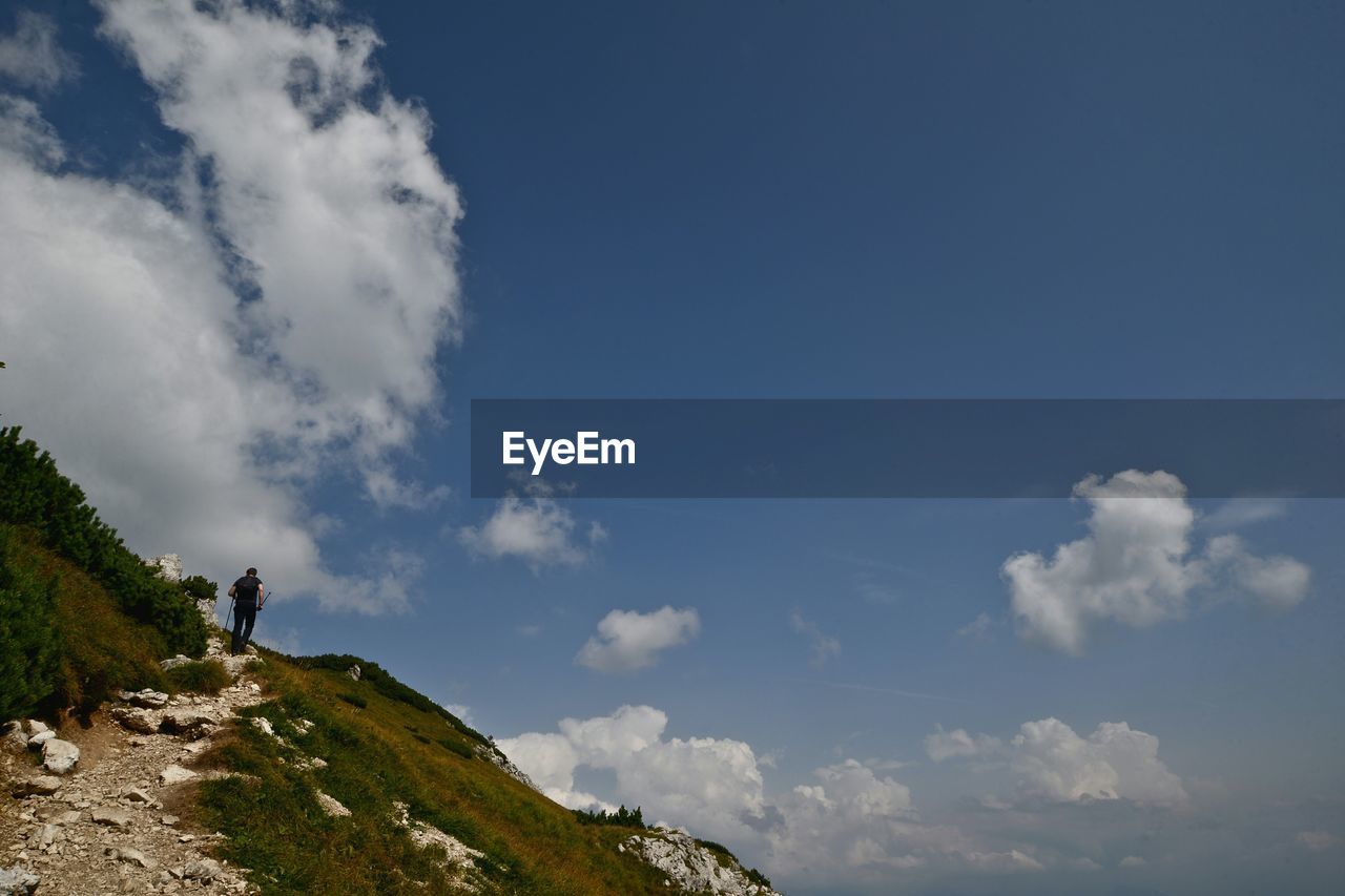 Low angle view of man standing on cliff against sky