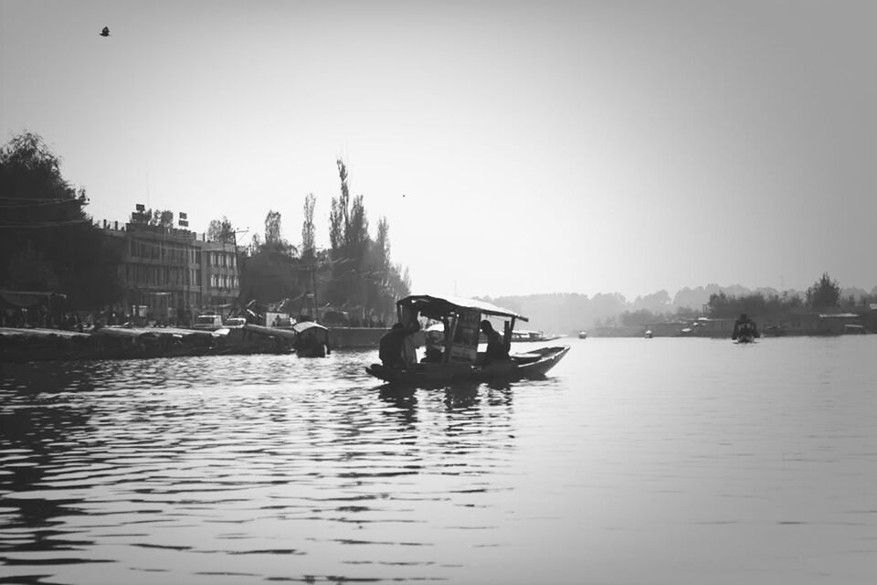 BOATS IN RIVER WITH BUILDINGS IN BACKGROUND AGAINST CLEAR SKY