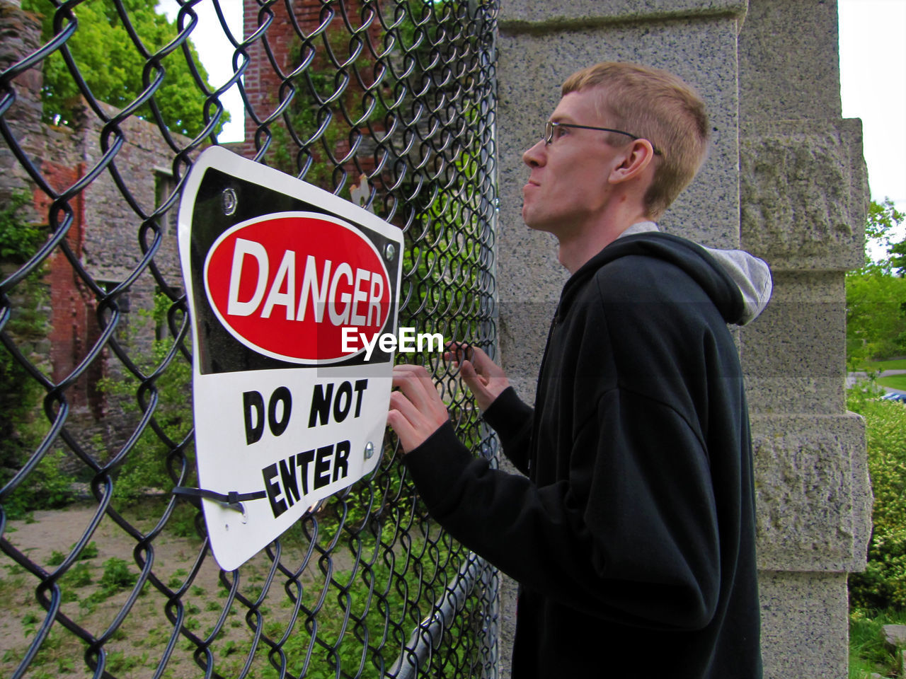 Side view of man standing by chainlink fence with do not enter sigh board