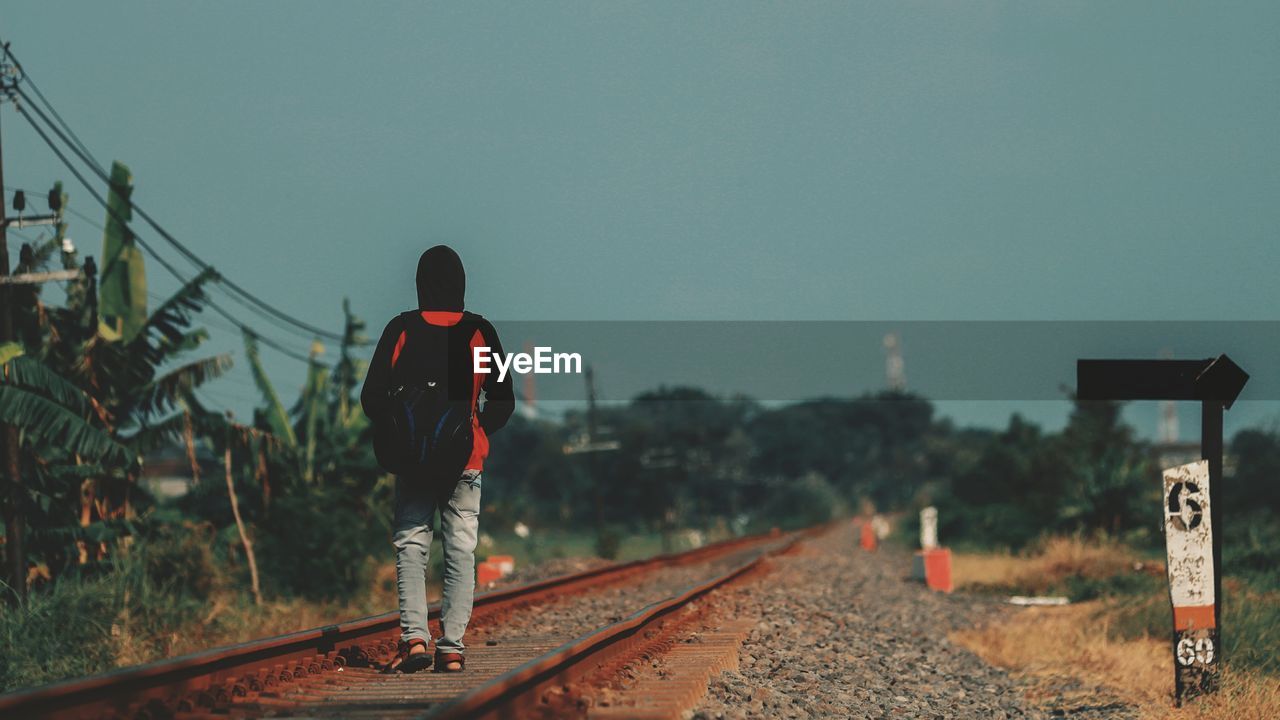 Rear view of man on railroad tracks against clear sky