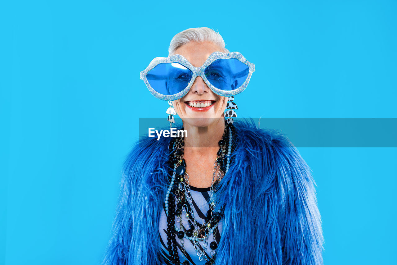 portrait of smiling young woman wearing sunglasses while standing against blue background