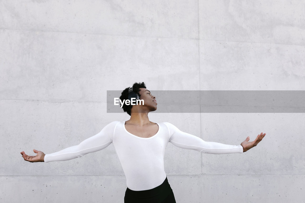 Young male dancer with arms outstretched doing rehearsal against white wall