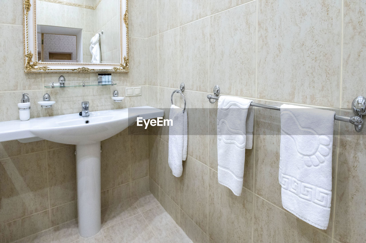 Bathroom with white sink and toilet white bathrobes for guests hang on the wall.