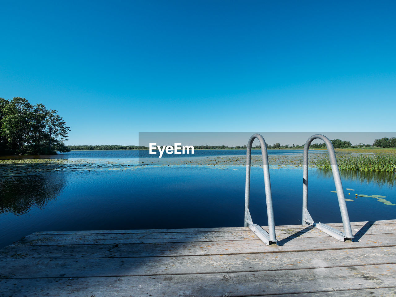 Swimming pool by lake against clear blue sky