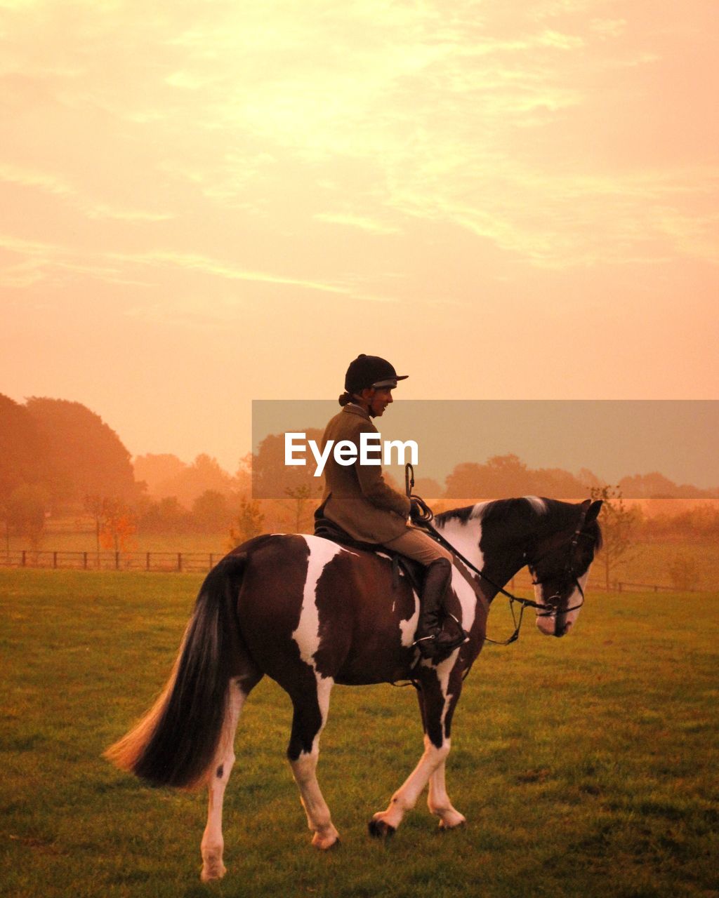 Woman riding on horse at field against sky during sunrise