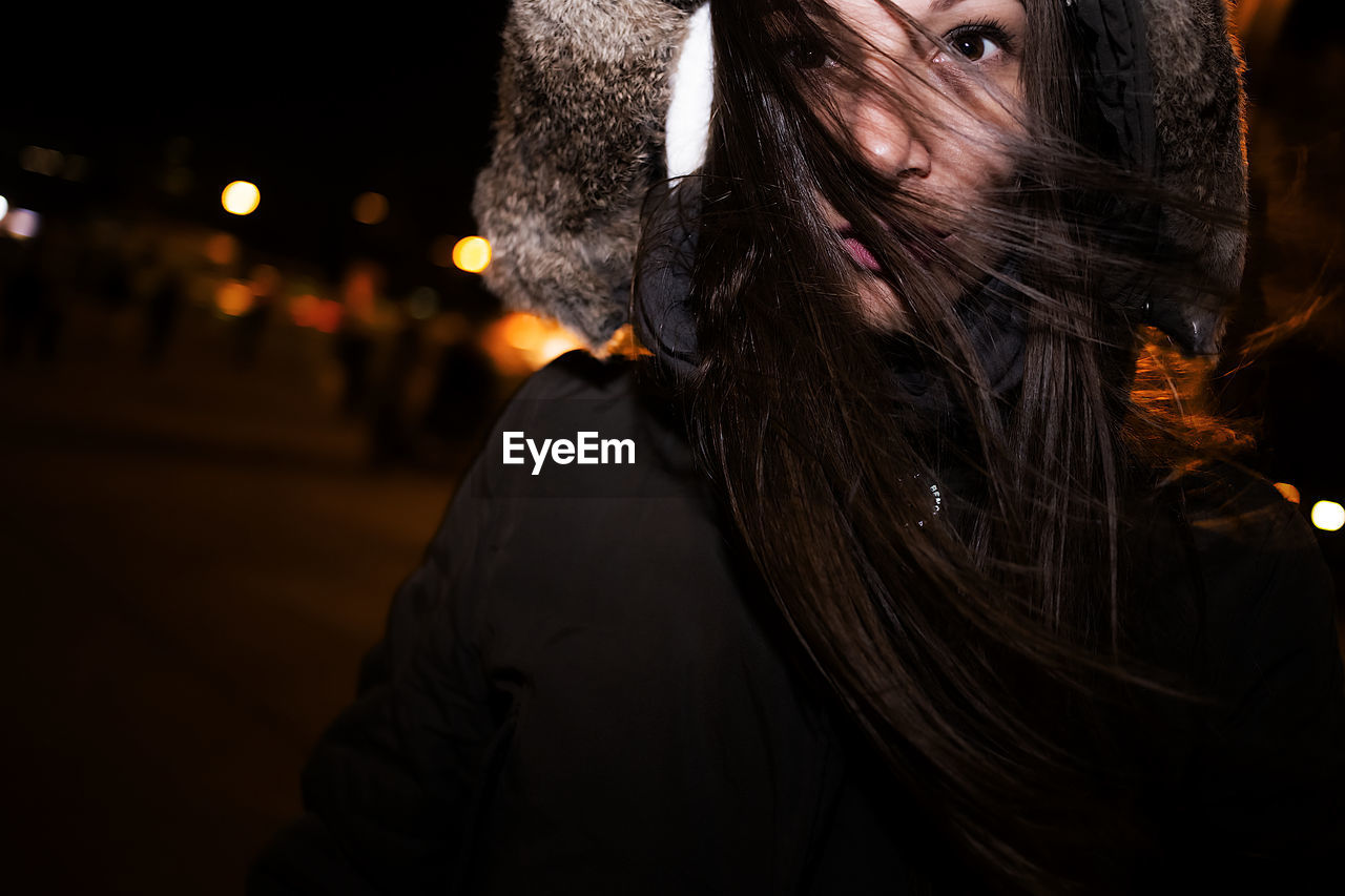 Thoughtful young woman wearing hooded jacket at night