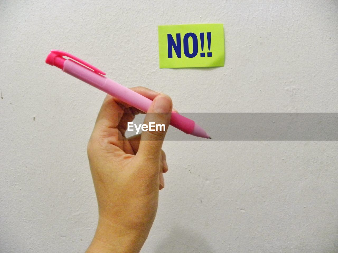 Cropped hand holding pen by adhesive note with no text on wall