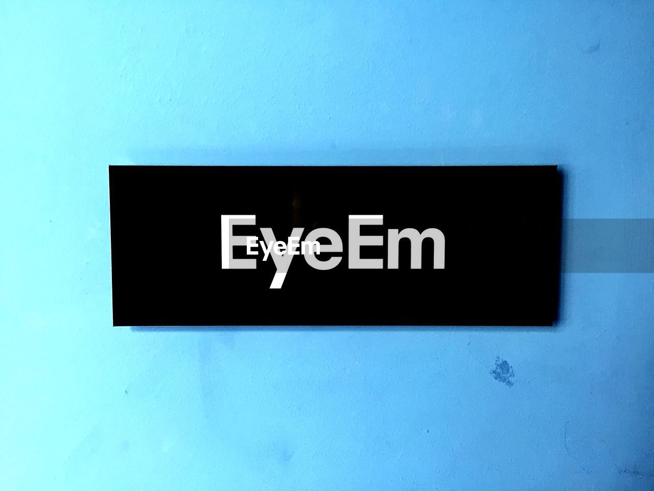 Close-up of eyeem sign on blue wall
