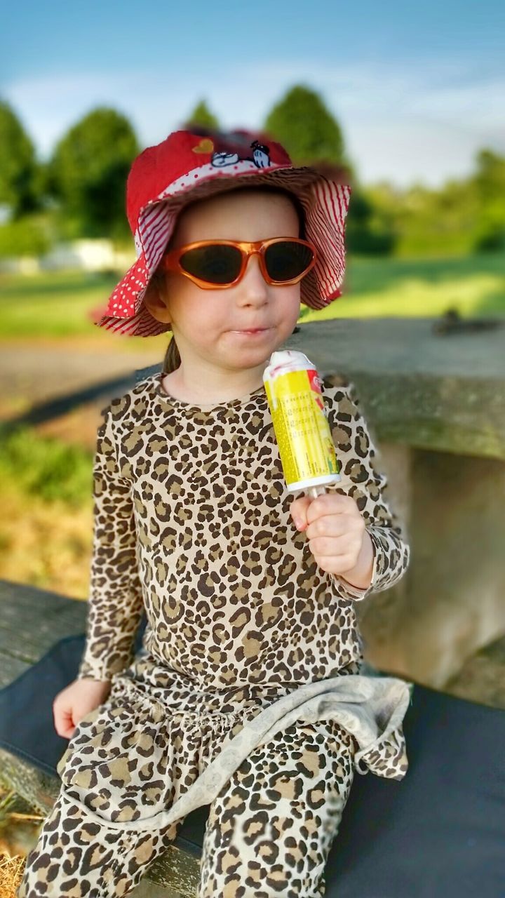 Cute girl in leopard print clothing having ice cream on railing