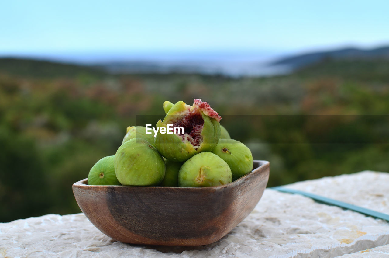 Wooden bowl with fresh, sweet, juicy figs with a mediterranean landscape in a background