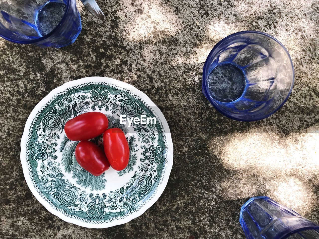High angle view of tomatoes on a plate on stone table with blue glasses
