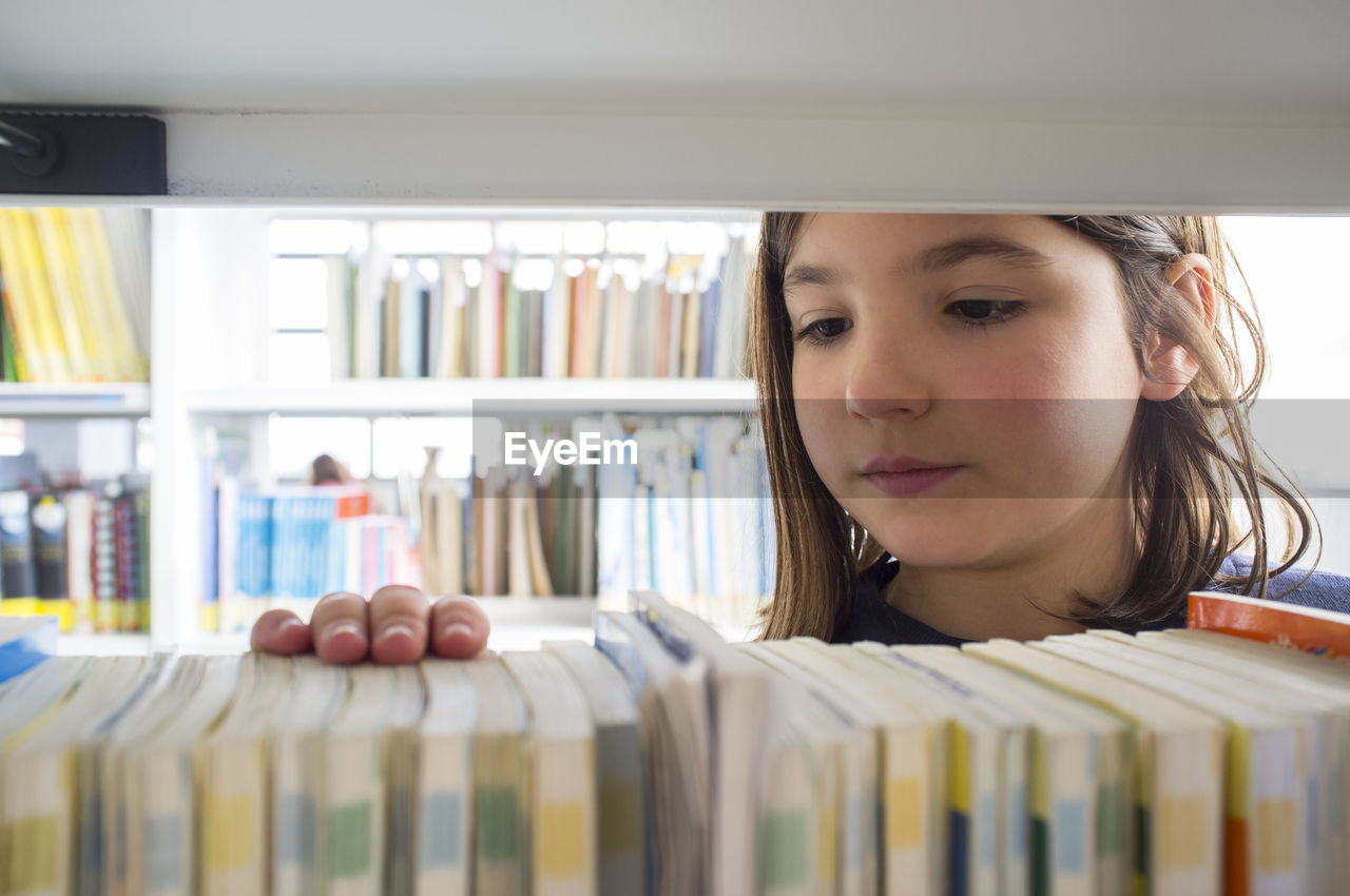 Young girl selecting books from library bookshelf