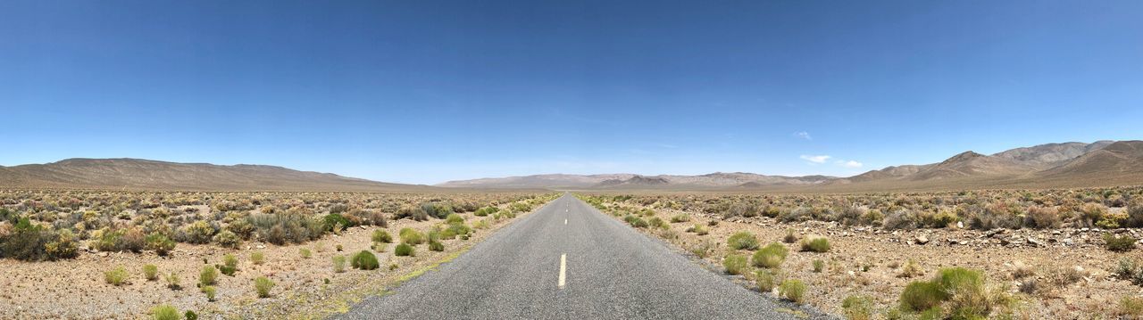 Panoramic view of road leading towards mountains against clear sky