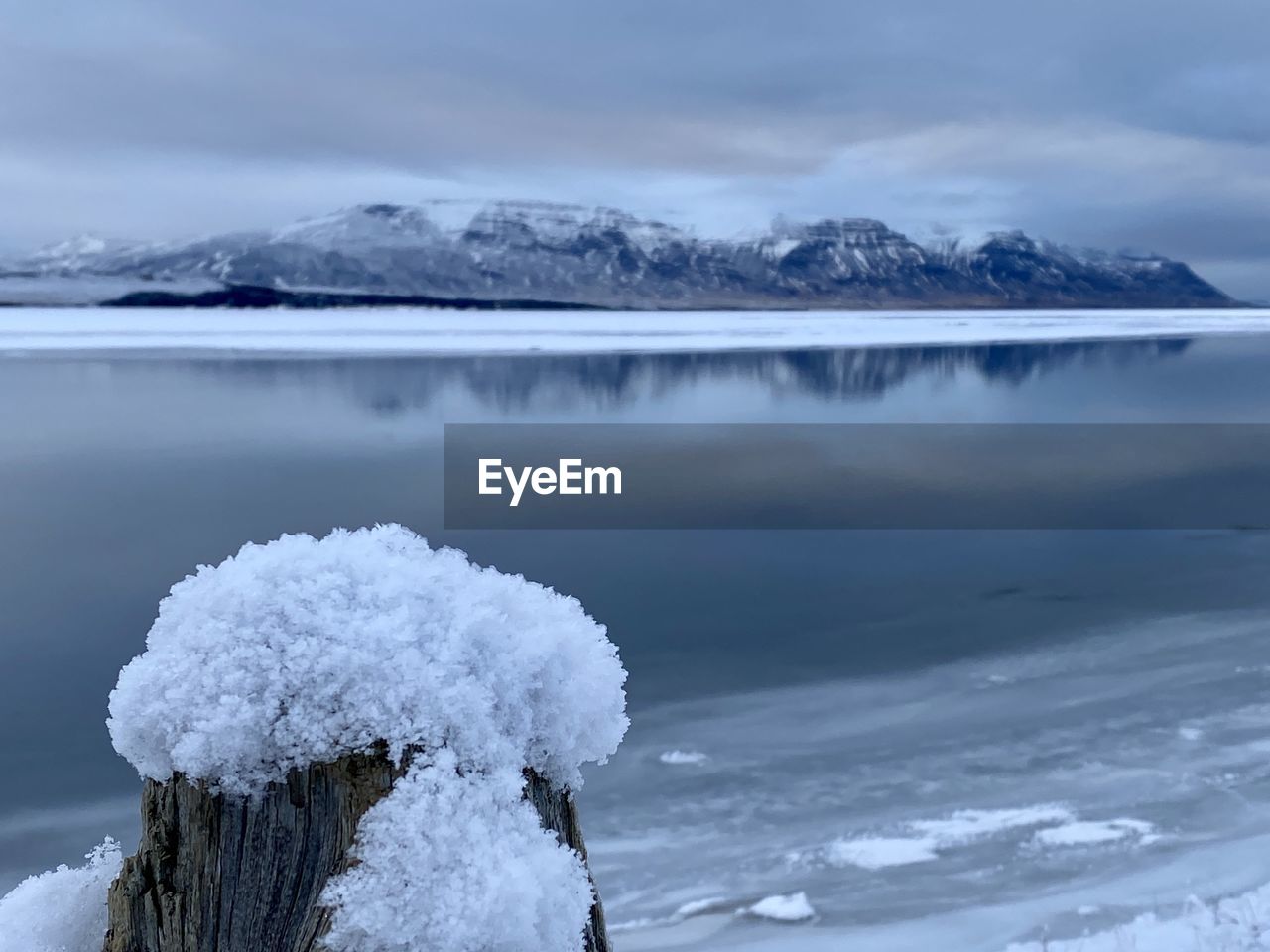 Frozen lake by snowcapped mountain against sky
