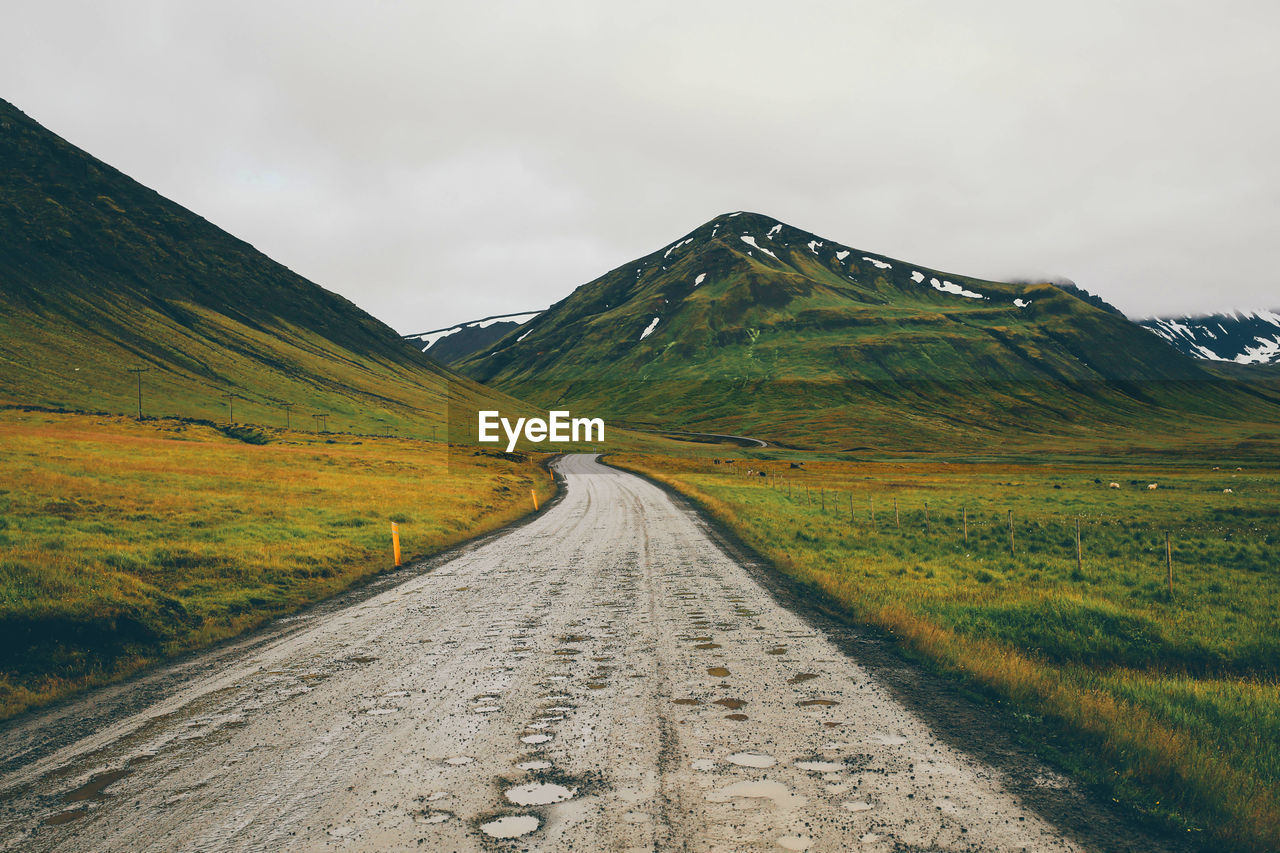 Empty road leading towards mountains against sky