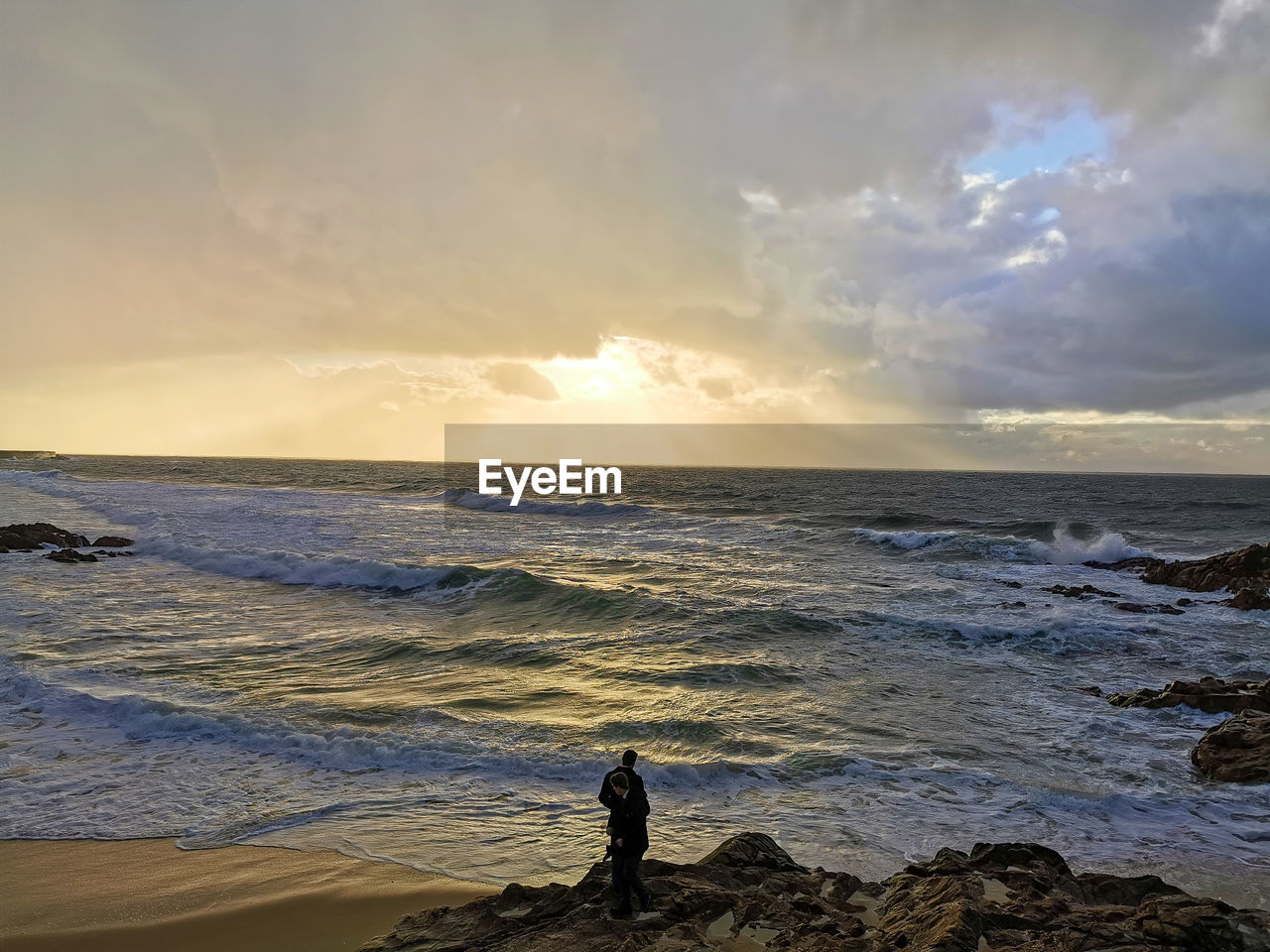 WOMAN STANDING ON BEACH AGAINST SKY DURING SUNSET