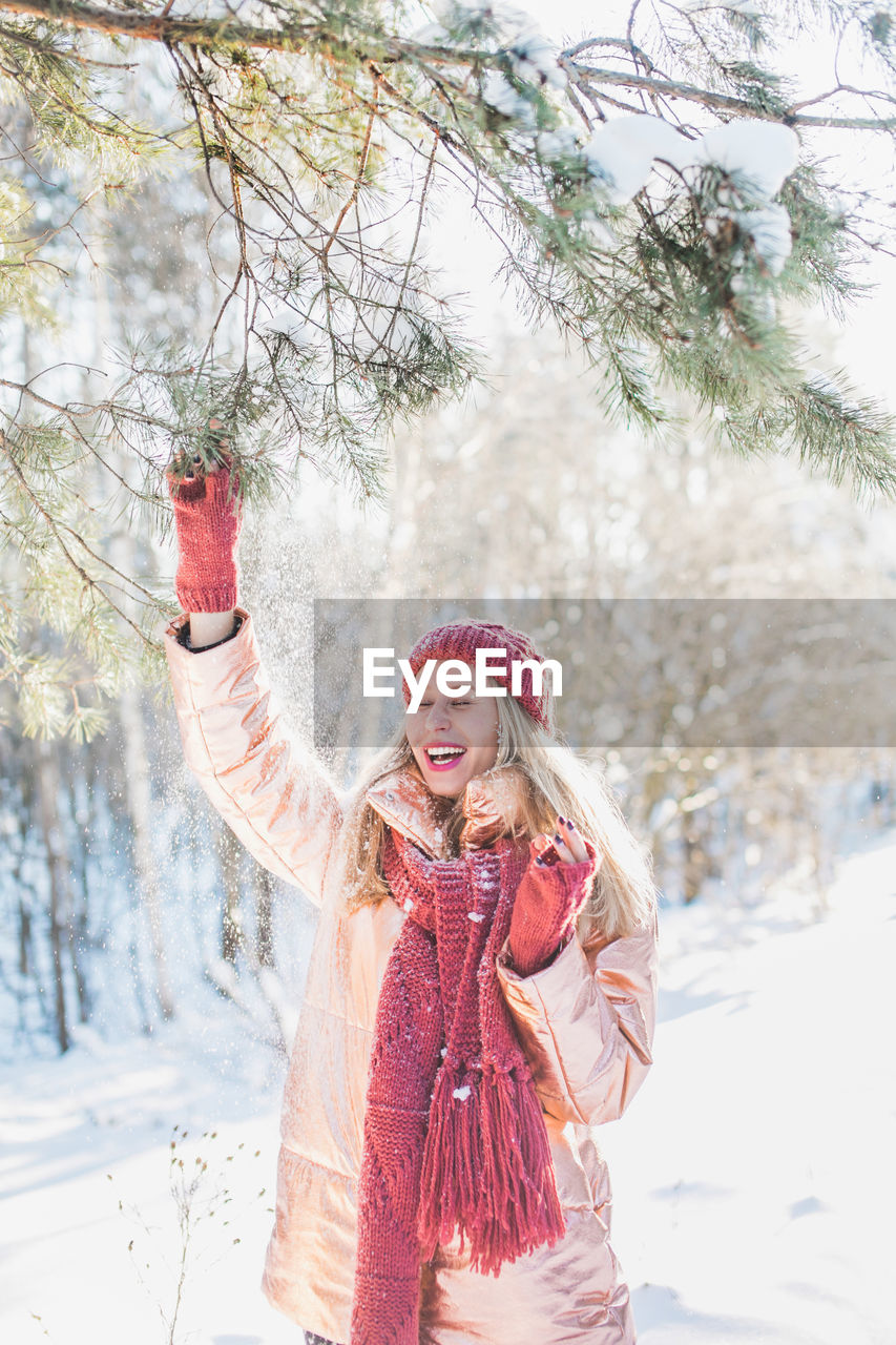 Happy young woman enjoying by trees on snowy field in winter