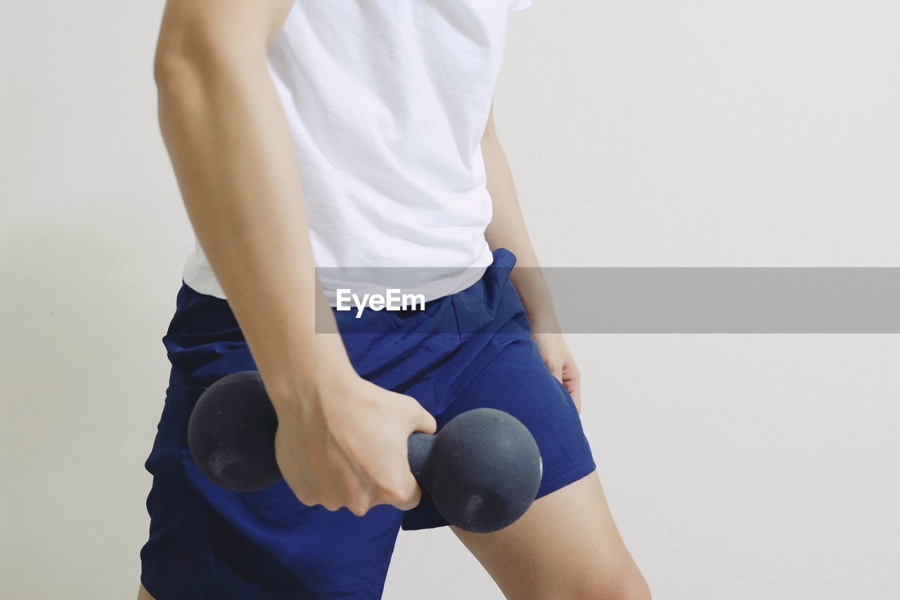 Midsection of man holding dumbbell while standing against wall