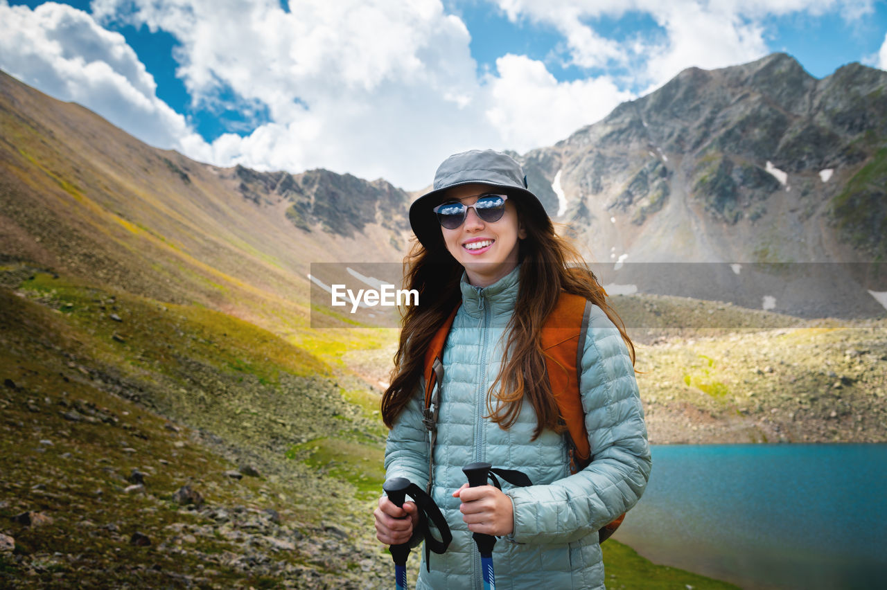 Smiling, positive girl with disheveled hair against the background of a blue mountain lake, with