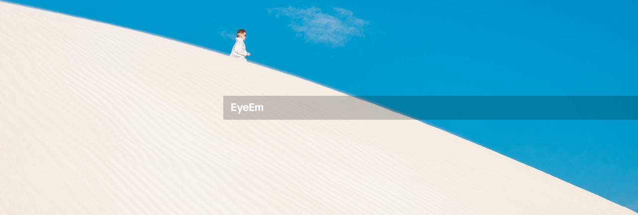 Low angle view of woman standing on sand dune against sky