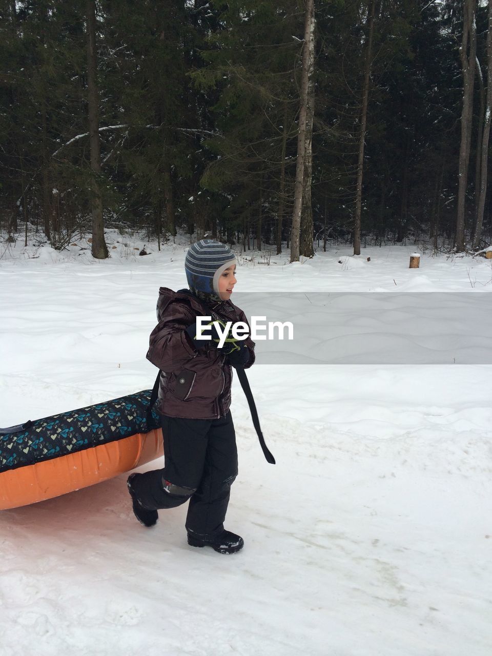 Full length of boy pulling snow tube on field during winter