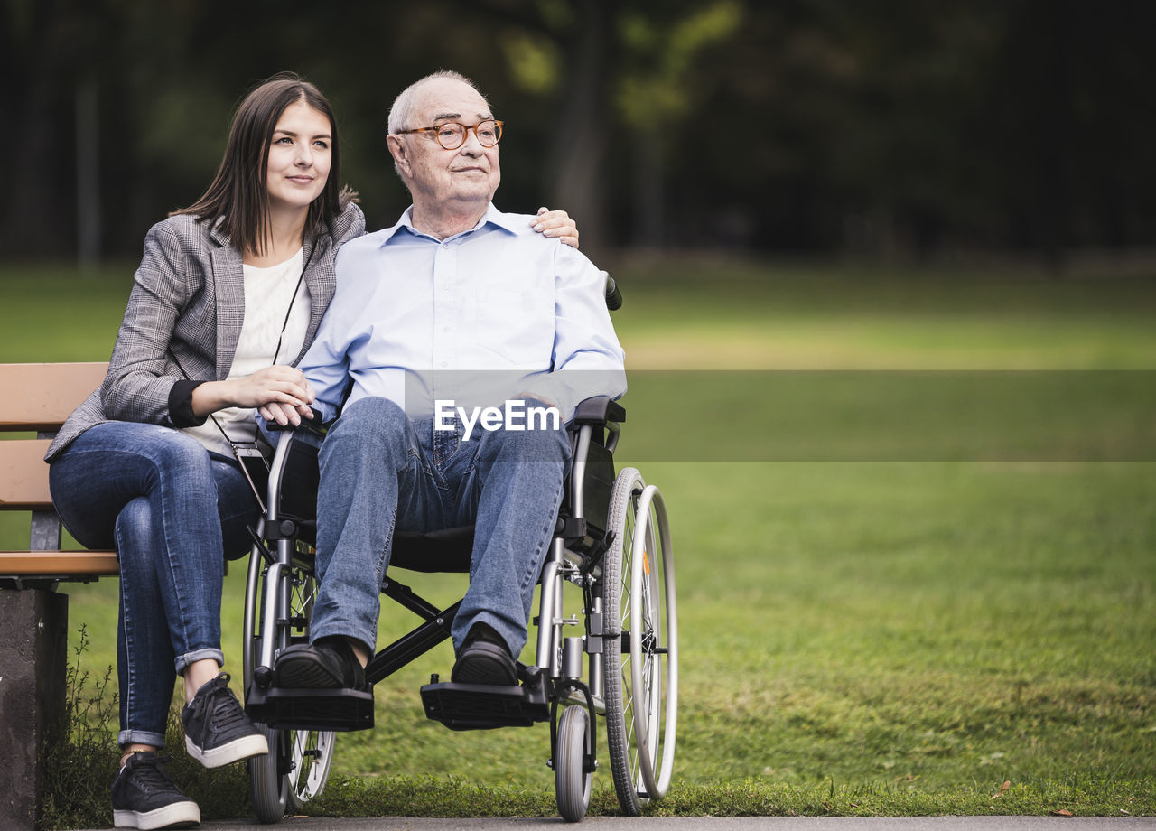 Portrait of senior man in a wheelchair relaxing with granddaughter in a park