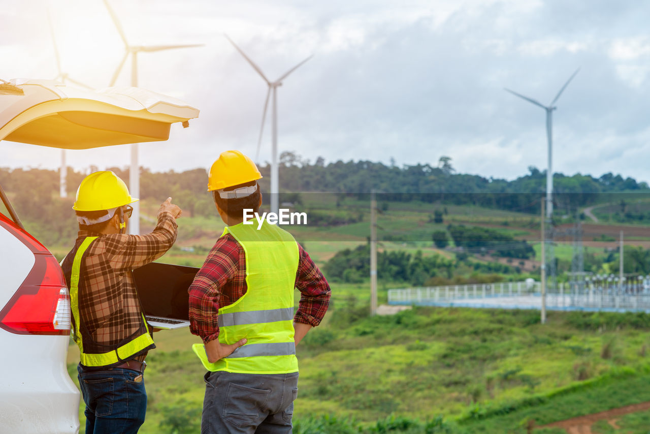 Rear view of man pointing towards windmill by colleague on land