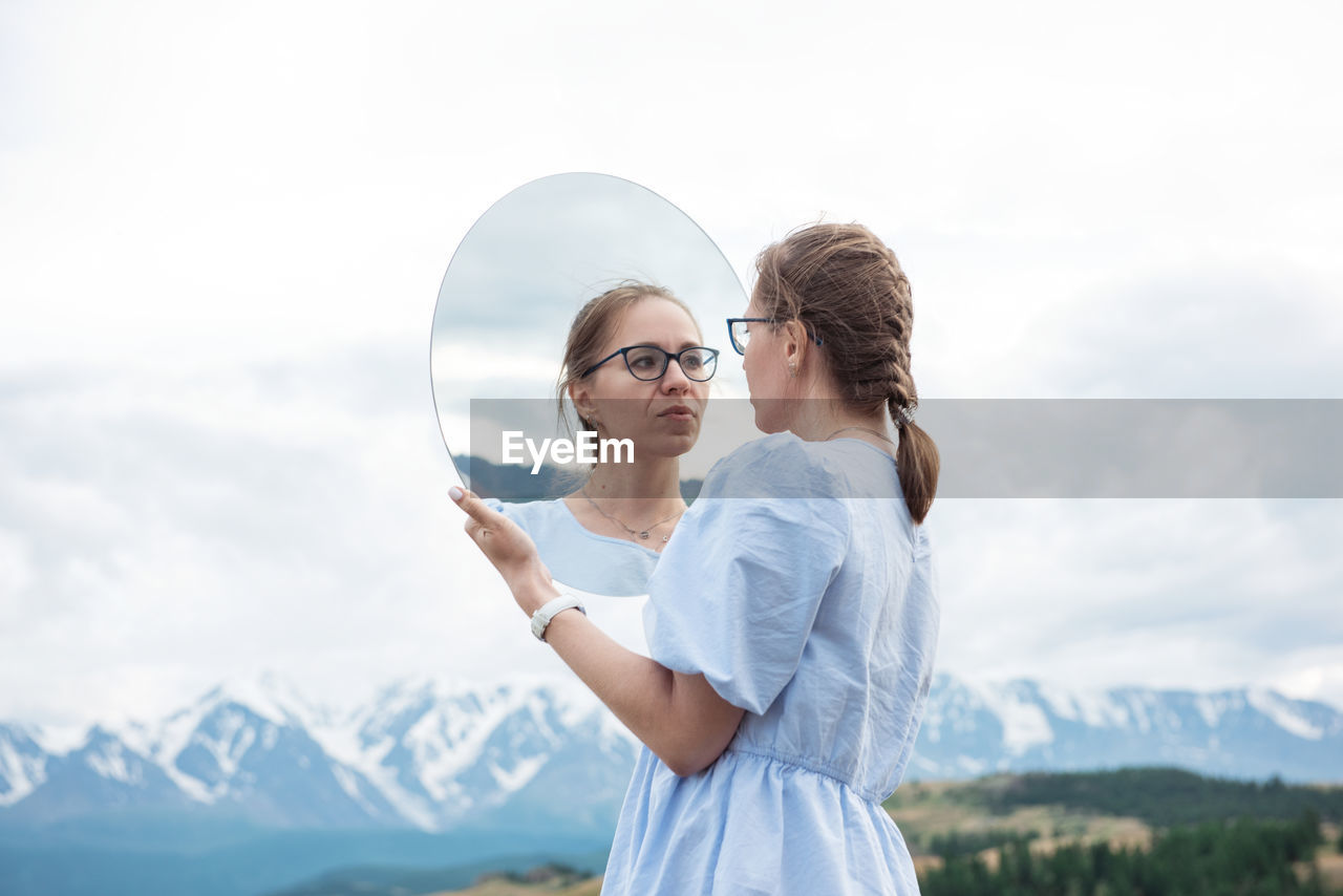 YOUNG WOMAN STANDING AGAINST MOUNTAIN AND SKY