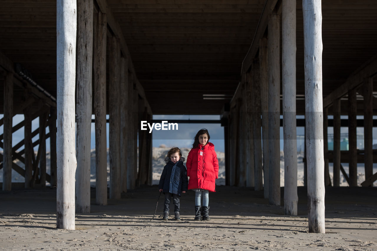 Full length of siblings standing under bridge at beach