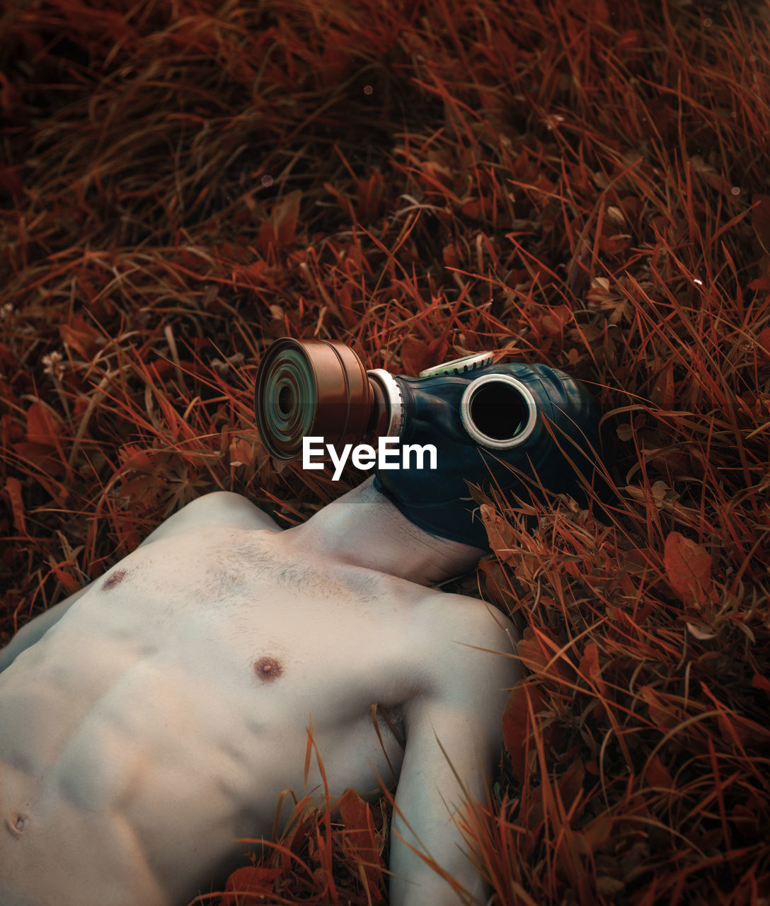 Shirtless man wearing gas mask while lying on grassy land