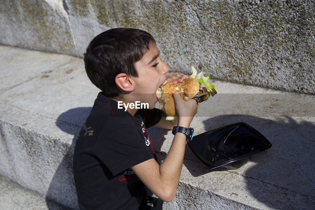 High angle view of eating burger by wall