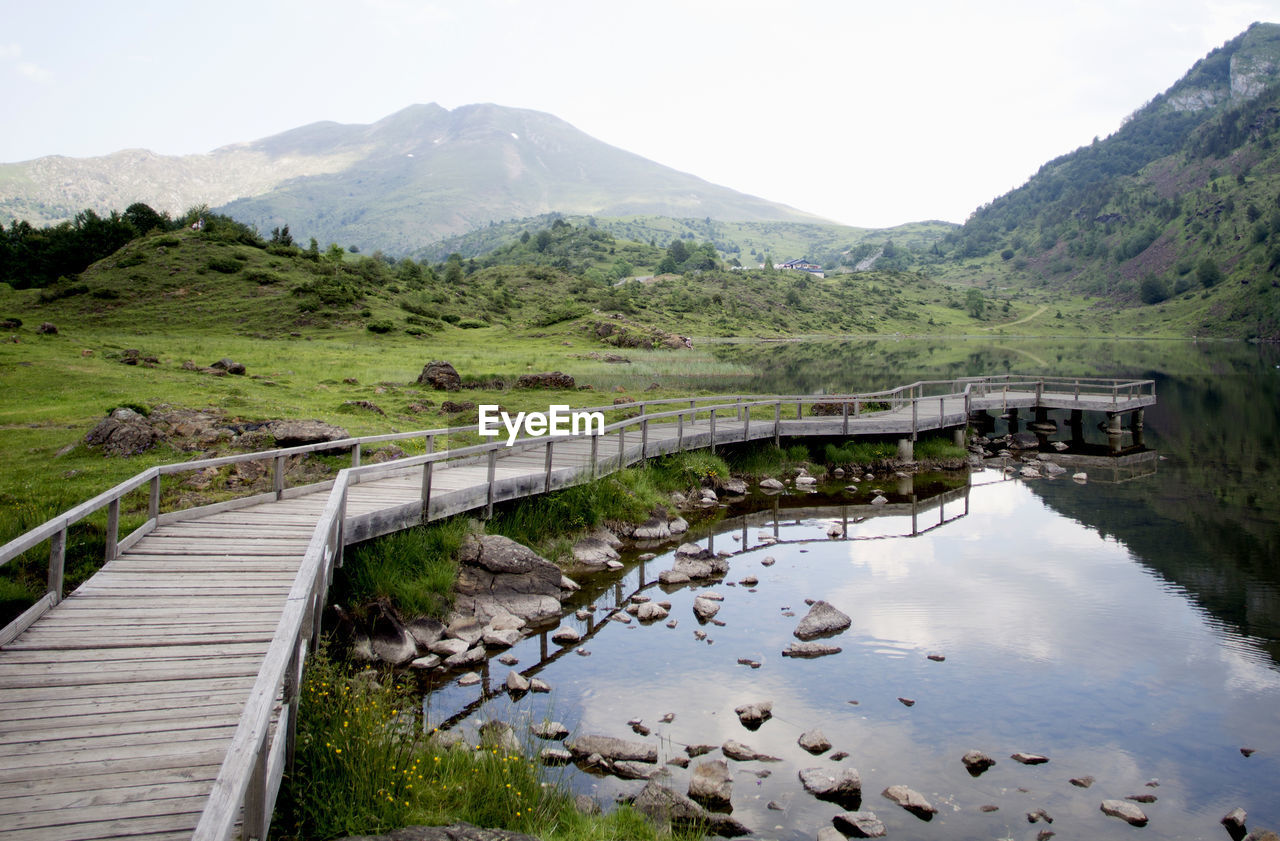 Wooden boardwalk by lake with mountains against sky