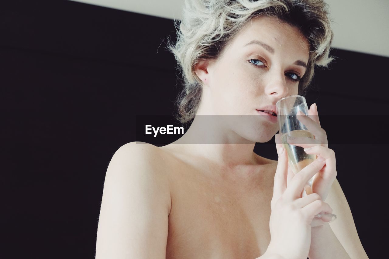 Portrait of topless woman drinking champagne at home