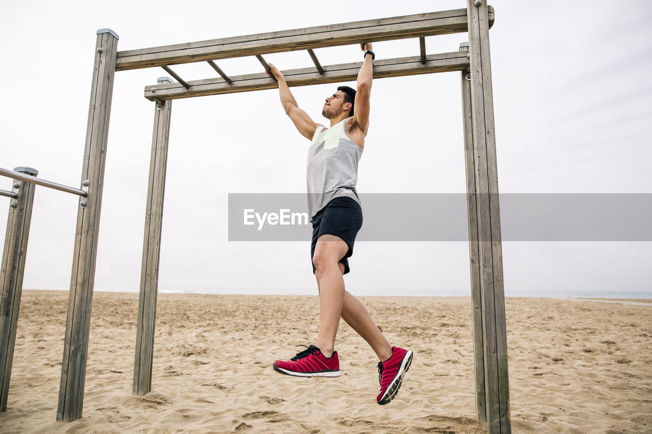 Young man exercising on monkey bars on the beach