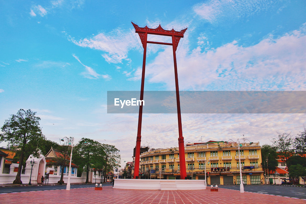 Low angle view of cross amidst trees and buildings against sky