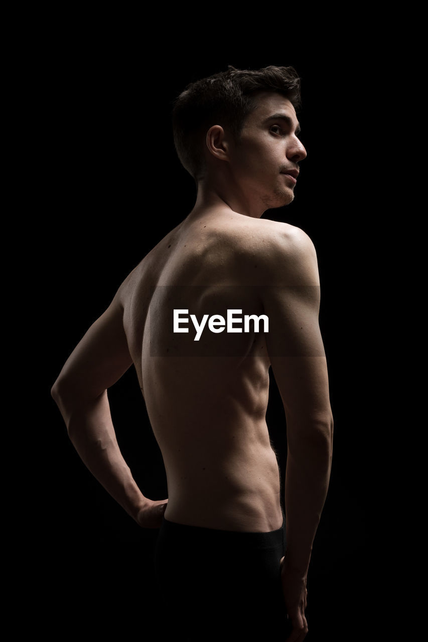 Shirtless man standing against black background