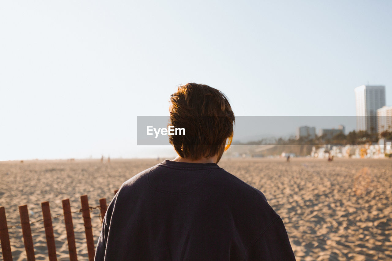 REAR VIEW OF MAN LOOKING AT SEA